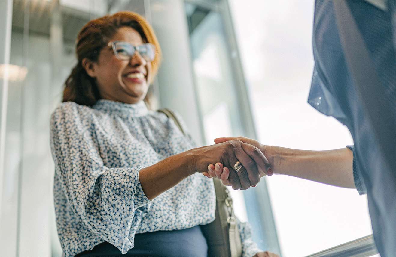 Smiling businesswoman with glasses shaking hands with a colleague in an office lobby.